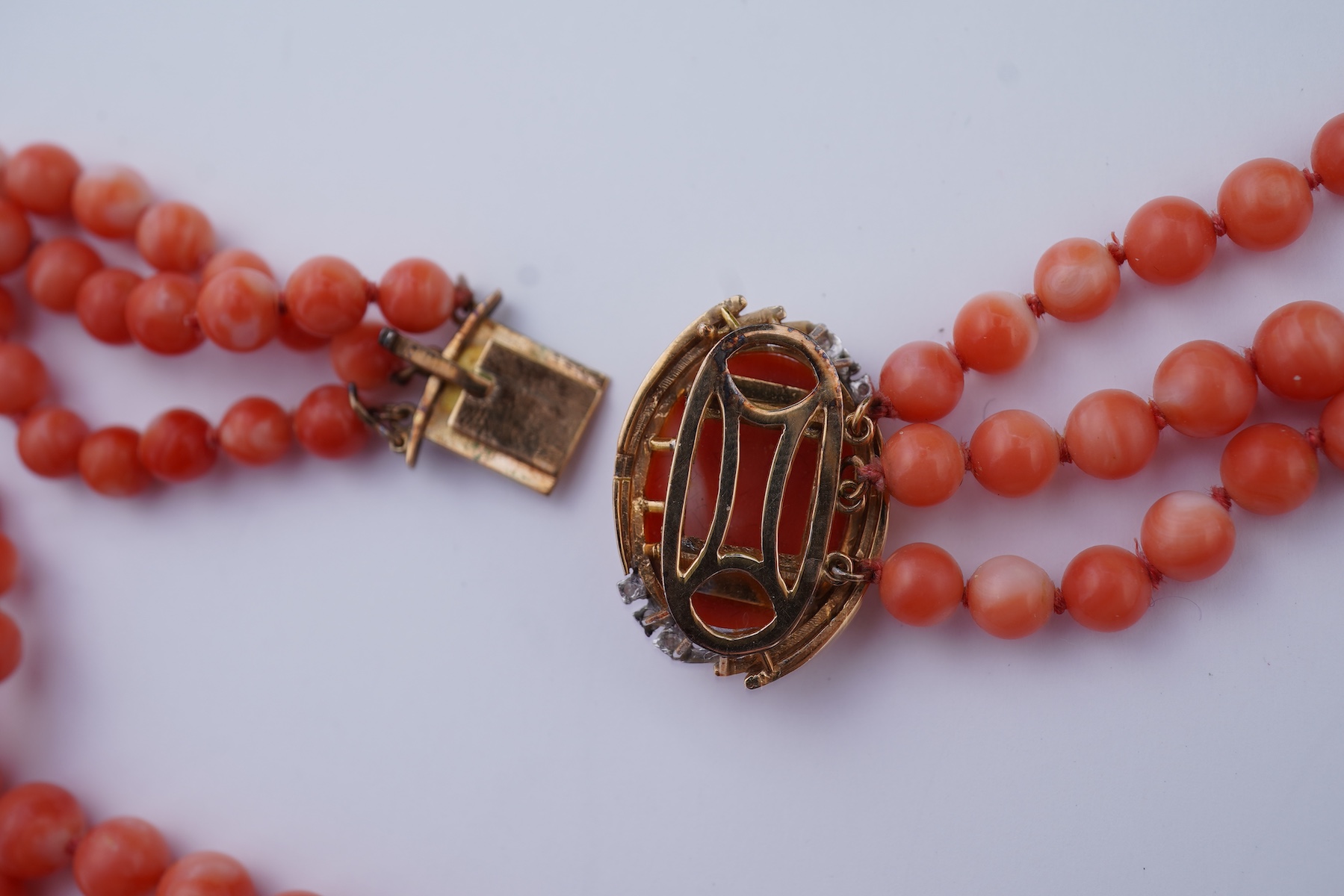 A coral necklace, composed of three strands of coral beads measuring approximately 5.1-6.6mm diameter, to a gold clasp set with a coral cabochon and brilliant-cut diamonds, mounted in gold, length 45.5cm, stamped 14K, ca